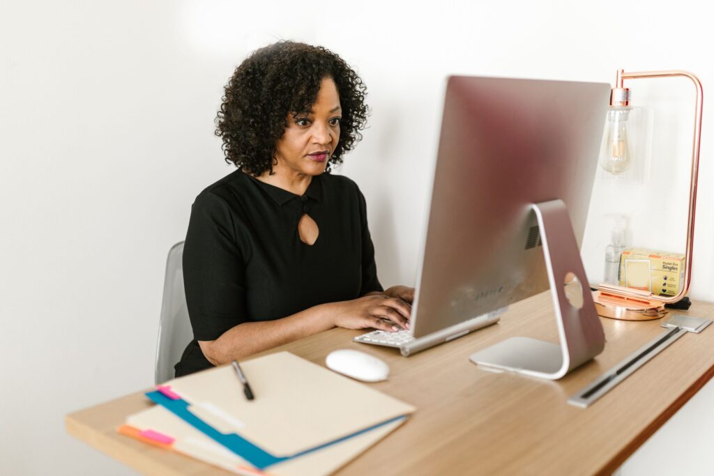 Office administrator working at her desk on a computer, with files and folders beside her